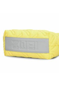 Bolso acolchado amarillo con un acento de cuero gris suave que presenta texto en relieve. Forma rectangular, patrón texturizado en la tela.