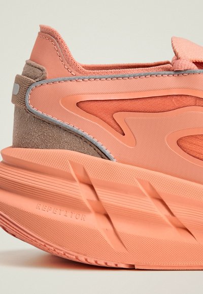 Chaussure de sport en suède pêche texturé et matériaux synthétiques lisses. Présente une semelle épaisse, de grands accents de logo et des coutures grises.