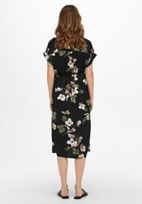 Abito nero floreale con maniche corte, dotato di una cintura e di un design fluido. La stampa mostra fiori bianchi e rosa con foglie verdi.