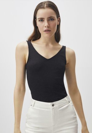 Zwarte geribbelde tanktop met een V-halsontwerp, voorzien van dunne bandjes. Gekocht in combinatie met witte high-waisted broek met knoopdetails.
