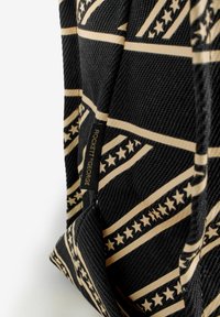 Fekete szövet táska texturált felülettel, vízszintes arany csíkokkal és csillagmintákkal. Tartalmaz egy "ROCKETT & GEORGE" feliratú címkét.