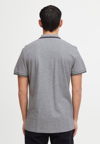 Šedé polo tri�čko s krátkými rukávy, límečkem a kontrastním černým lemováním na rukávech. Měkká tkanina s hladkým povrchem. Minimalistický design.