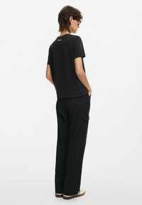 Camiseta de algodón negra con un corte relajado, mangas cortas y un pequeño logotipo en la parte posterior. Combinada con pantalones cargo negros que cuentan con bolsillos.