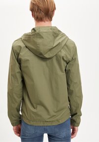 Leichte olivegrüne Jacke mit Kapuze, elastischen Bündchen und gerafftem Saum. Glattes Material mit einem subtilen Glanz, minimalistisches Design.