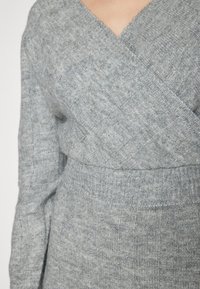 Maglione grigio lavorato a maglia con un design incrociato, vita a costine e un motivo testurizzato con dettagli di tessitura variabile.