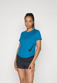 Teal Sport-T-Shirt mit kurzen Ärmeln, abgerundetem Saum und schwarzem Nike-Logo-Detail. Kombiniert mit schwarzen Shorts mit elastischem Bund.
