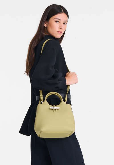 Green leather handbag with a rounded top, detachable shoulder strap, and silver hardware accent on the front. Textured finish.