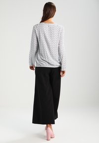 Haut à manches longues blanc à motif de points noirs, associé à un pantalon large noir et des talons compensés roses. Tissu lisse, coupe décontractée.