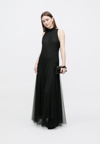 Black gown with a high neck, sleeveless design, and sheer lace overlay. Accompanied by a small black clutch. Smooth fabric texture.