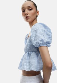 Blau-weiß karierter Puffärmel-Oberteil mit gerafftem Mieder und Peplum-Saum. Getragen mit weißen, elastischen Bundhosen im minimalistischem Design.