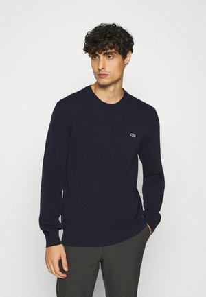 Navy long-sleeve sweater made of soft fabric, featuring a crew neck and a small embroidered green logo on the chest.