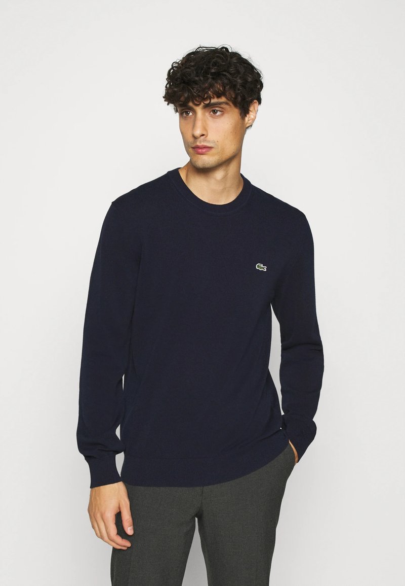Navy long-sleeve sweater made of soft fabric, featuring a crew neck and a small embroidered green logo on the chest.