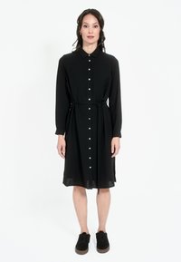 Must mustaga, pikad varrukad, nööpidega ees, vööt puusas ja midi pikkus, koos tumedate kingadega. Sile tekstuur.