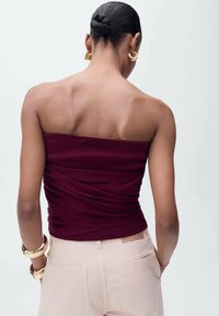 Bordeaux strapless top met een geribbelde textuur en een verzameld ontwerp aan de achterkant, gecombineerd met lichtroze op maat gemaakte broek en gouden ronde oorbellen.