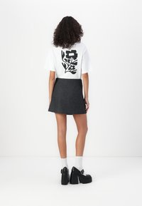 White t-shirt with a black floral design on the back, paired with a dark gray fabric skirt and black chunky-heeled shoes.