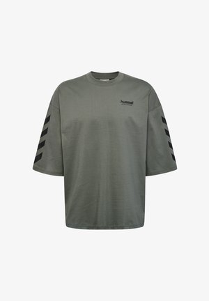 Olivgrön oversized t-shirt i bomull med rundad halsringning. Har svarta chevron-mönster på ärmarna och en liten logotyp på bröstet.