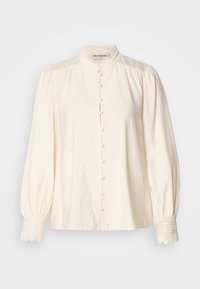 Camicia bianca con colletto alto, chiusura anteriore con bottoni e maniche a sbuffo. Presenta un bordo in pizzo sui polsini e un tessuto leggermente testurizzato.