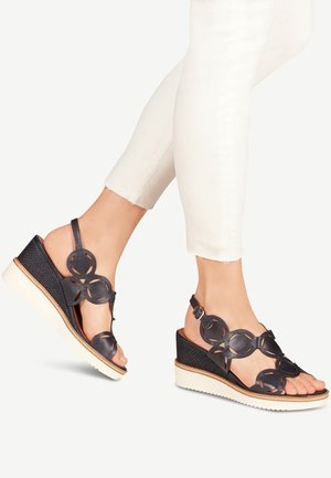 Zwarte leren wedge-sandalen hebben uitgesneden bloemenaccenten, een gestructureerde hak, een verstelbare enkelband en een witte rubberen zool.