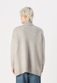 Lys grå strikket genser med høy krage, ribbestrikkede mansjetter og en teksturert finish. Lengre bak, med en avslappet passform.