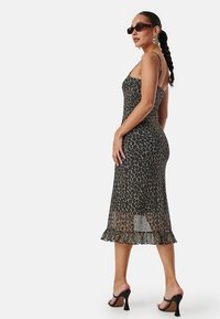 Midi šaty s leopardím vzorem, tenkými ramínky, průsvitnou tkaninou, rozšířeným spodním okrajem a volánkovým lemem. Stylizováno s otevřenými podpatky a slunečními brýlemi.