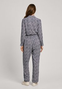 Cvečni kombinezon z dolgimi rokavi, ki ima poudarjen pas in široke hlačnice. Temna podlaga z majhnimi roza in belimi cvetličnimi vzorci.