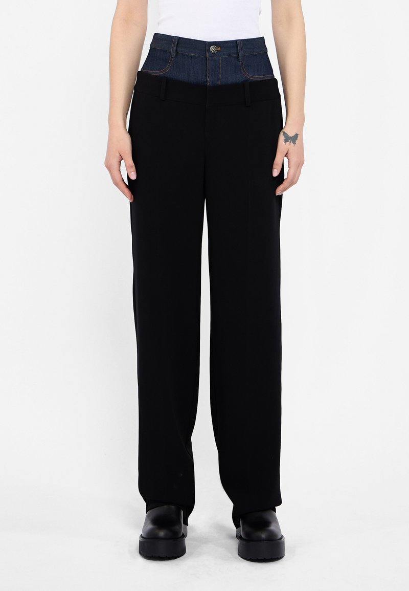 High-waisted pants featuring a dark denim band, black wide-leg fabric, front pockets, and a single button closure with contrast stitching.