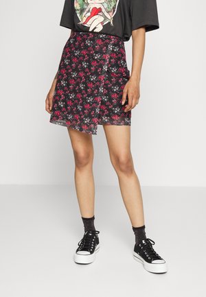Saia preta com flores vermelhas e brancas, apresentando um design cruzado. Combinada com uma t-shirt gráfica e sapatilhas pretas.
