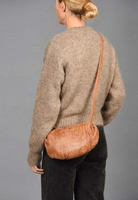 Bolso de hombro de cuero marrón con una superficie suave y texturizada y una forma redondeada; llevado cruzado con una correa a juego, combinado con un suéter de punto.