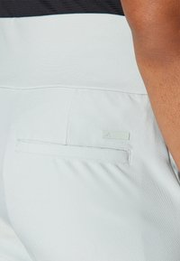 Světle modré kalhoty s plochou zadní kapsou a obdélníkovou etiketou, vyrobené z hladkého, pružného materiálu se jemnou texturou.