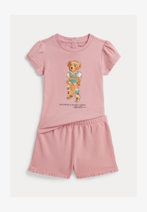Rózsaszín két részes baba szett rövid buggyos ujjú felsővel, amelyen ruhába öltözött medve illusztrációja látható, és hozzáillő fodros rövidnadrág.