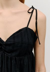 Zwarte jurk van een textuurstof met verticale strepen. Het heeft dunne verstelbare bandjes en een geraffineerde bodice.