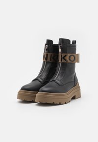 Zwarte leren enkellaarzen met een dikke bruine zool, voorzien van dubbele zijritsen en een brede beige band met verhoogde letters.