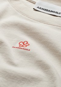 Beige katoenen t-shirt met een klein rood geborduurd bloemenlogo en de tekst "ARMEDANGELS" nabij de halslijn. Zachte textuur, casual ontwerp.