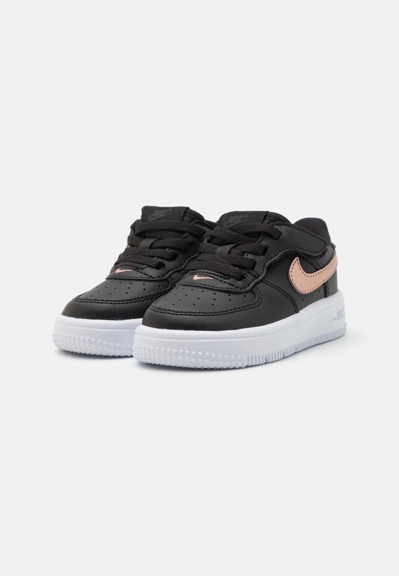 Baskets en cuir noir avec un orteil perforé, semelle en caoutchouc blanche et swoosh Nike en rose gold. Comprend des lacets noirs et des détails cousus.