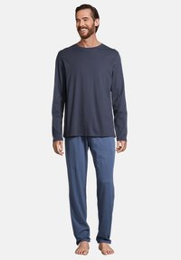 Camicia a maniche lunghe blu navy realizzata in un tessuto morbido con scollatura a girocollo, abbinata a pantaloni larghi di colore azzurro chiaro in un materiale morbido simile.