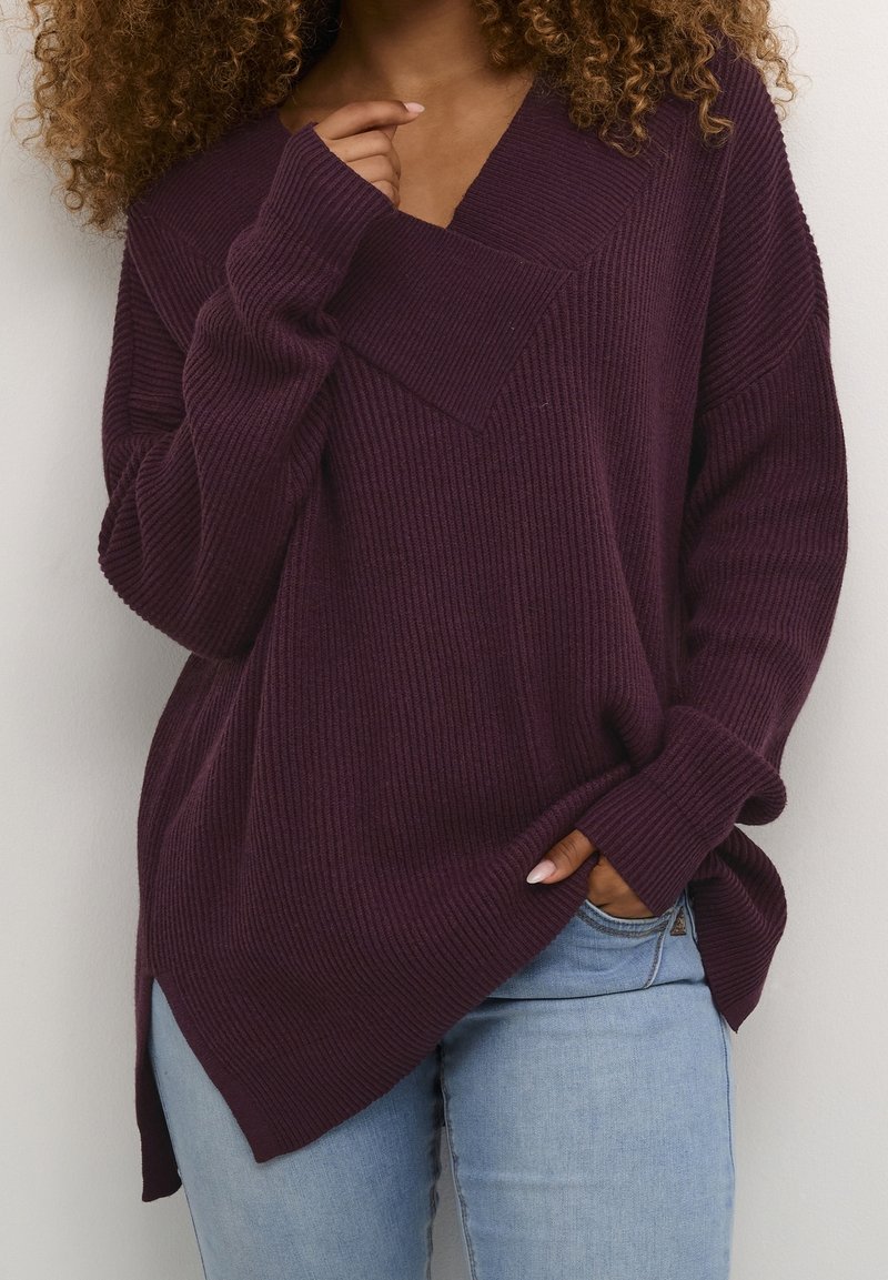 Mysig, oversized, ribbad stickad tröja i djup lila med V-hals och sidoflikar, ihop med ljusblå jeans.