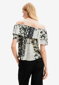 Blusa off-the-shoulder con strati arricciati, motivi floreali in verde e nero, tessuto leggero e vestibilità comoda.