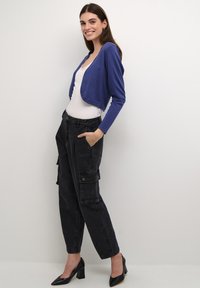 Blue cropped cardigan over a white top, paired with high-waisted black cargo pants featuring side pockets, worn with black heeled shoes.