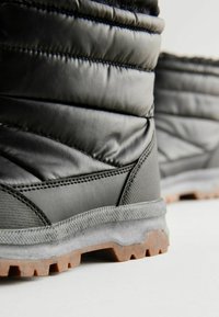 Bottes noires rembourrées avec un dessus texturé, semelle en caoutchouc et un intersemelle gris distinct. Les caractéristiques incluent des coutures détaillées et un motif adhérent.