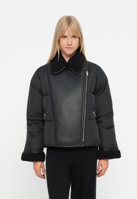Sort pufferjakke med faux shearling krave og manchetter, udstyret med en shiny læderpanel og asymmetrisk lynlås.