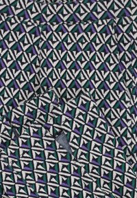 Textiel met een geometrisch patroon van driehoeken in zwart, wit, paars en teal, met een gestructureerde stoffen afwerking en contrasterende kleuren.