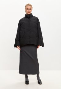 Czarna kurtka puchowa z wysokim kołnierzem, długimi rękawami i poziomym przeszyciem. Połączona z szarą spódnicą i czarnymi butami.