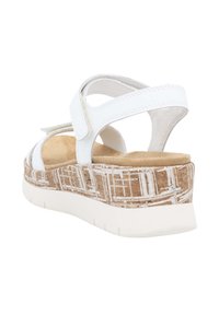 White sandals with adjustable straps, a cushioned insole, and a patterned cork wedge sole with a white rubber bottom for traction.