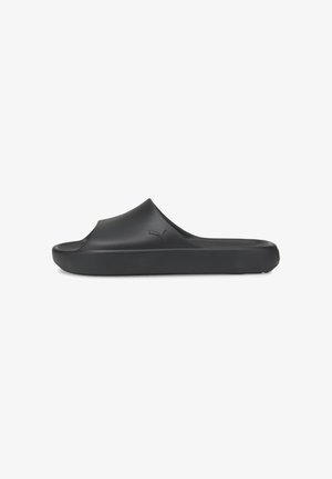 Sandale slip-on noire Puma avec orteils ouverts, semelle épaisse et logo Puma embossé sur le côté, montrée en profil latéral sur fond blanc.