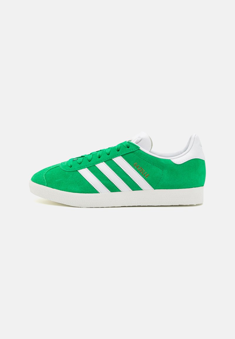 Green suede sneaker with white three-stripe design, white heel, and textured rubber sole. Features gold "Gazelle" branding on the side.