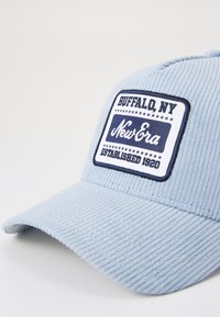 Gorra de pana azul claro con visera curva, que presenta un parche rectangular azul marino que dice "Buffalo, NY" y "New Era" en texto blanco y azul.