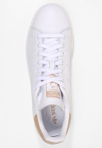 Vit lädersneaker med rund tå, platt snördesign, beige hälaccent och logotyp på tungan. Slät yta genom hela skon.