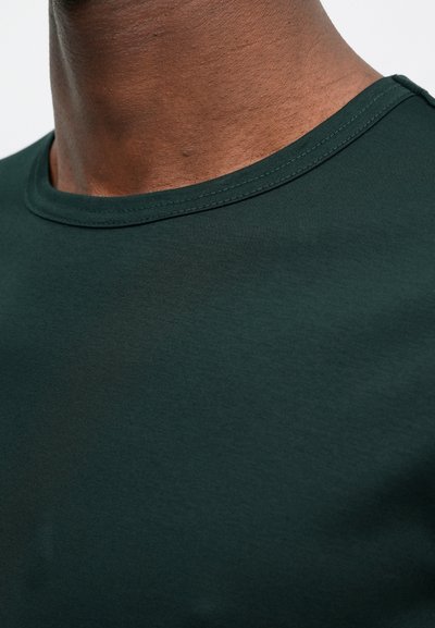 Σκούρο πράσινο μπλουζάκι crewneck, κοντινή λήψη. Λείος βαμβακερός ύφασμα με κανονική εφαρμογή, με ριγέ λαιμόκοψη και διακριτές ραφές.