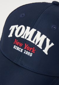 Namočná baseballová šiltovka z odolnej tkaniny s bielou vyšitou značkou "TOMMY", červeným nápisom "New York" a akcentom "SINCE 1985". Štruktúrovaný tvar so zakriveným šiltom.