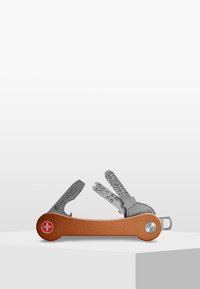 Multiverktyg nyckelhållare med kopparfinish, som har silverfärgade nycklar och ett litet blad, kompakt design med rund ände och logotypdetalj.